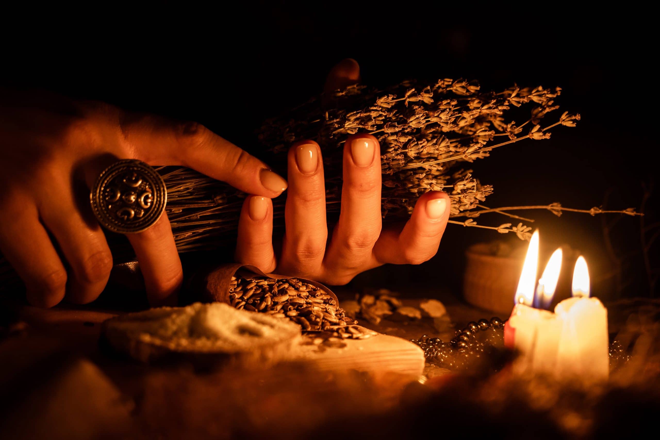 In the hands of the witches bunch of dry herbs for divination. The light from the candles on the old magic table. Attributes of occultism and magic.